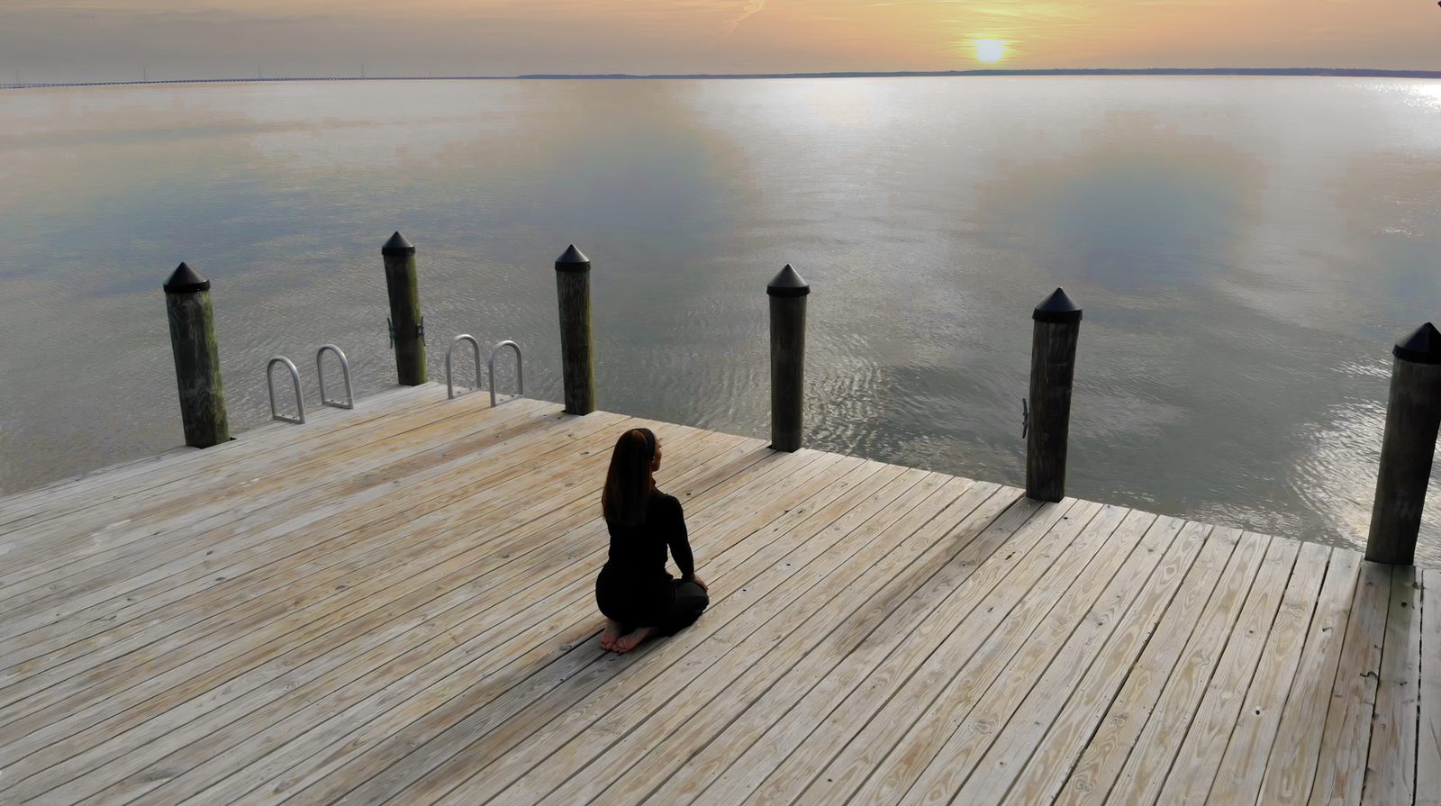 Carmen Kennedy seated on the dock at sunset, looking out over the James River